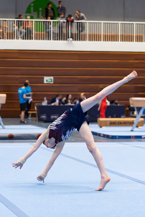 Gymnast performs cartwheel on floor mat with extended limbs during routine in indoor sports hall with spectators