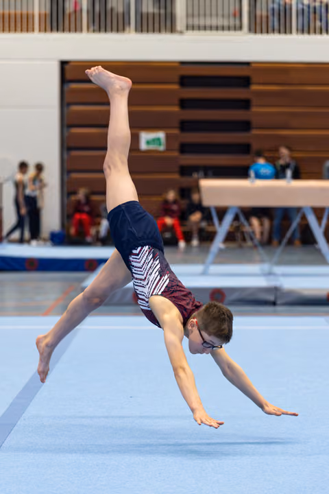 Young athlete performs a cartwheel on floor exercise at an indoor competition, showing impressive form and flexibility