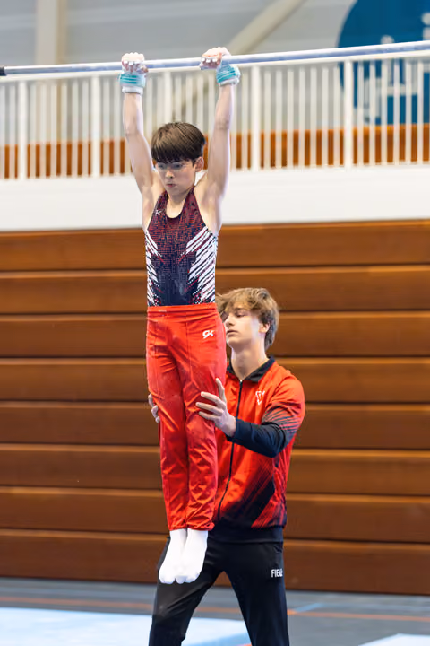 Young athlete performs handstand on bar while coach spots from behind, demonstrating trust and concentration during practice
