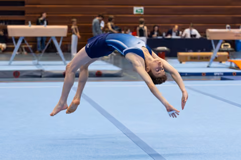 Athlete performing backward somersault mid-air during floor exercise routine at indoor championship event