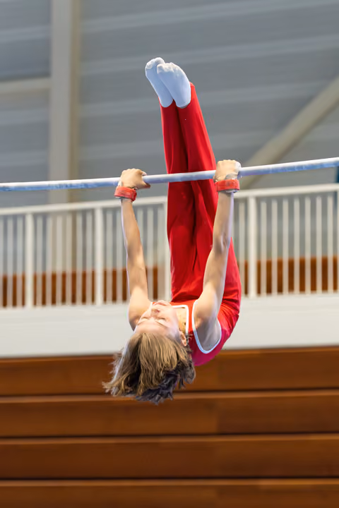 Athlete performs inverted hang on horizontal bar with pointed toes, displaying strength and control during routine