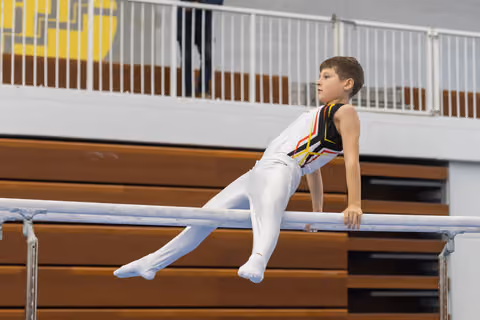 Young gymnast performs support position on parallel bars, body extended with focused expression in gymnasium