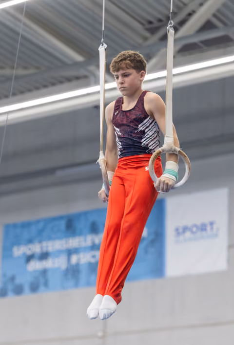 Young male gymnast performing on rings apparatus in training facility, displaying concentration and strength