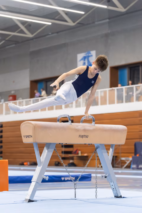 Young male gymnast performs a horizontal support position on pommel horse during training in indoor gymnasium
