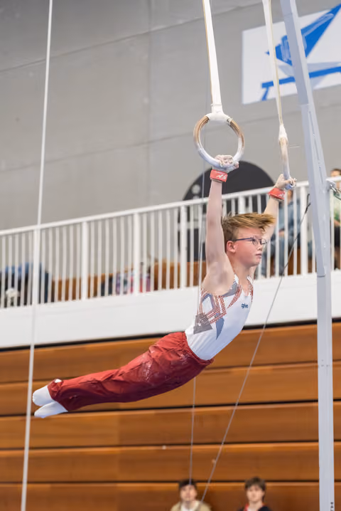 Young gymnast performing a horizontal hold on still rings, displaying focus and strength during his routine in an indoor gym
