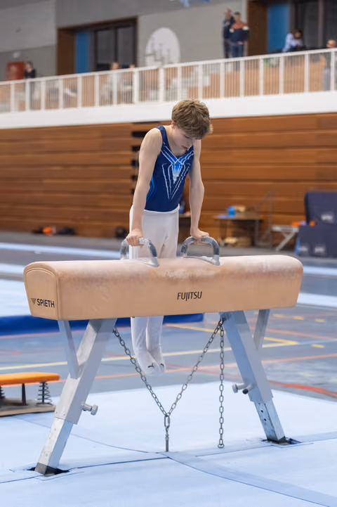 Young gymnast performing on pommel horse with focused concentration, hands gripping handles during indoor gymnastics practice