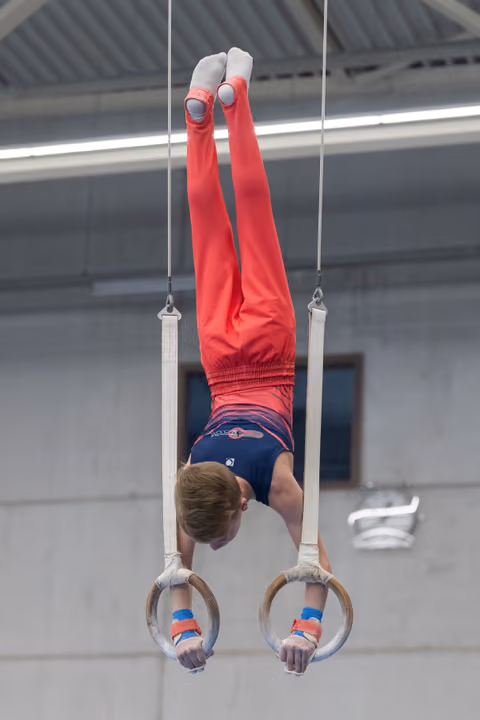 Male gymnast performing an inverted handstand position on still rings in an indoor training facility
