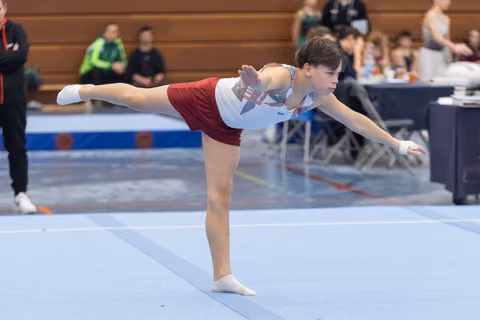 Young gymnast executes an arabesque balance on floor mat, demonstrating control and extension during routine