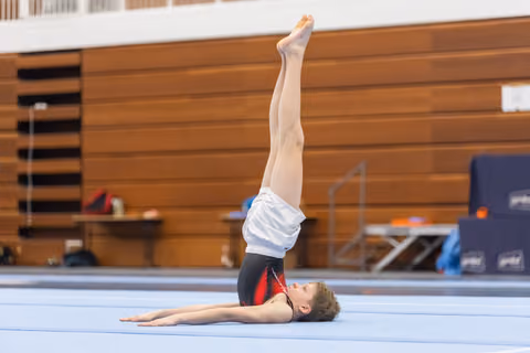 Young gymnast performs a controlled shoulder stand on the floor mat during training in an indoor sports facility