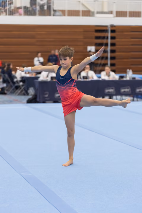 Young gymnast performs an arabesque balance on floor exercise, arms extended gracefully during her routine at indoor meet