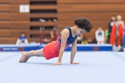 Young gymnast holds a plank position during floor routine, demonstrating strength and focus on competition mat