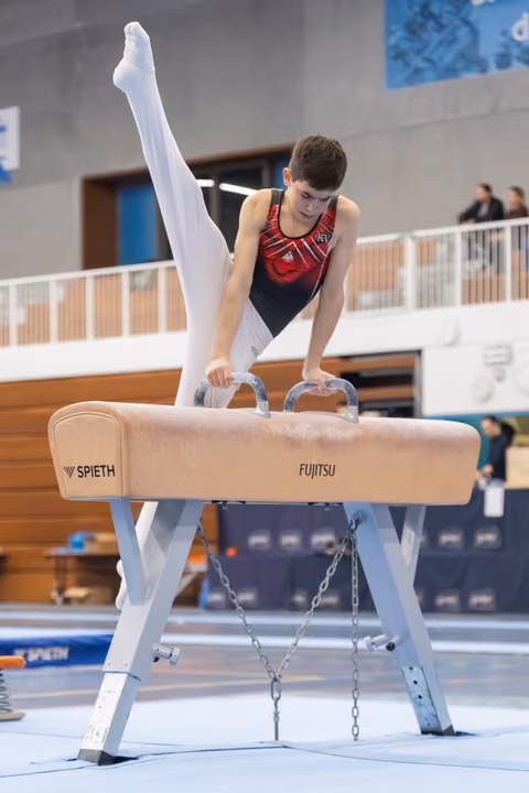 Male gymnast executing a straddle position on pommel horse, displaying strength and control during his routine