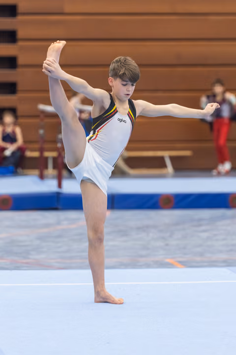 Young gymnast performs impressive vertical split balance on floor, demonstrating exceptional flexibility in white German team leotard