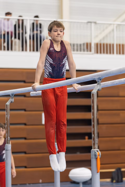 Young male gymnast performing on parallel bars wearing navy sequined leotard and red pants in indoor gym facility
