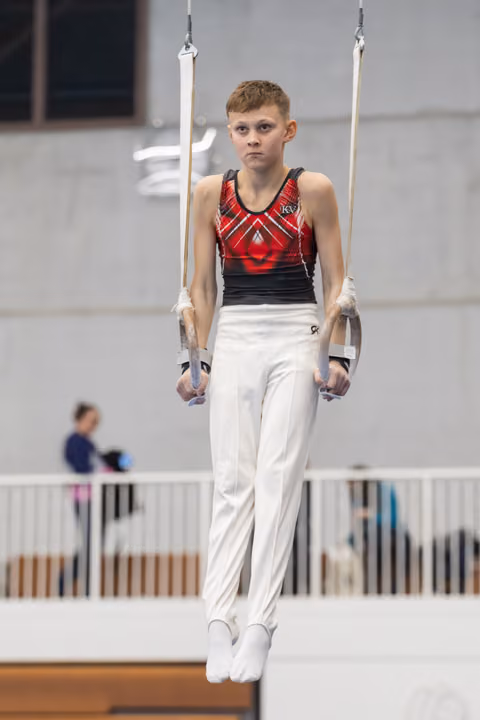 Young male gymnast performing on parallel bars, displaying intense concentration in white pants and red patterned leotard