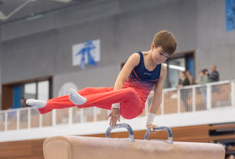 Young gymnast demonstrates strength and focus on pommel horse, executing a horizontal hold with legs extended
