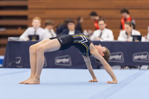Young gymnast performs a backward bridge pose during floor routine, arching body with hands and feet planted on mat