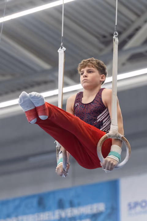 Young male gymnast performing L-sit position on rings, displaying intense focus and controlled strength in gymnasium