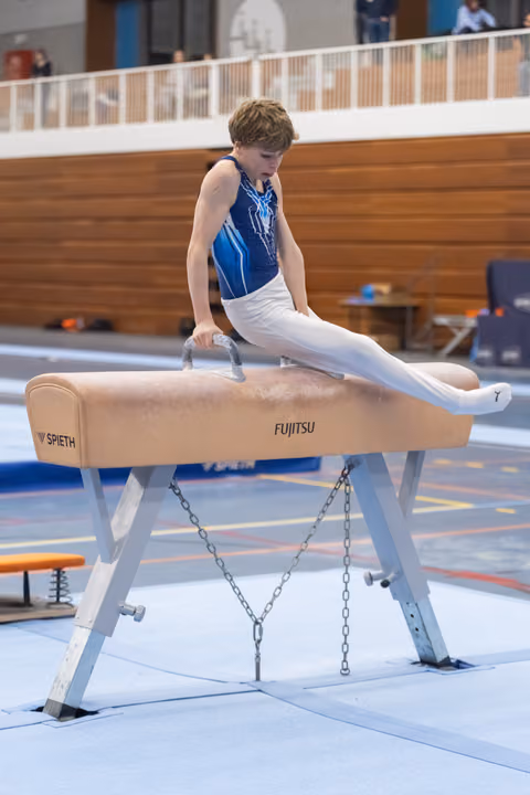 Young gymnast in blue leotard executes scissors skill on pommel horse, demonstrating control and leg extension during training