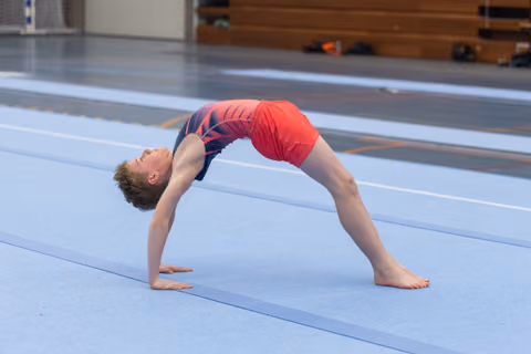 Young gymnast executing a deep backbend bridge on training floor, demonstrating remarkable flexibility and control