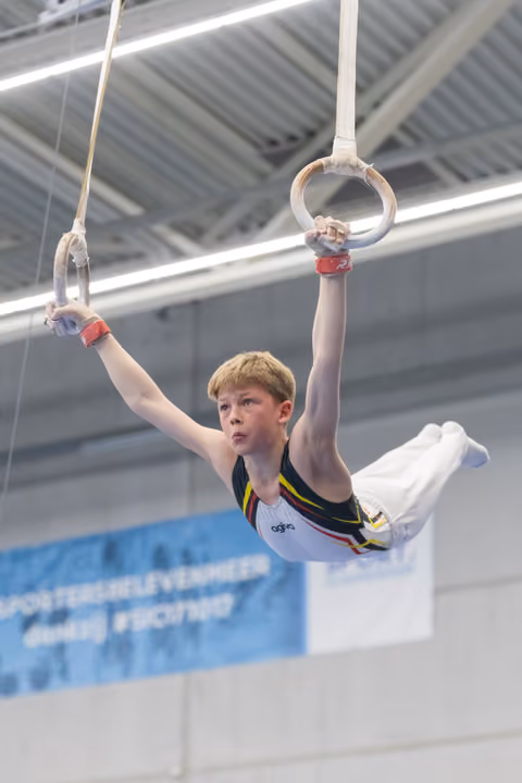 Young male gymnast performing on rings, displaying intense concentration while holding position in indoor training facility