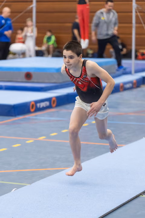 Young gymnast in red and black leotard landing on floor exercise mat with focused expression during routine