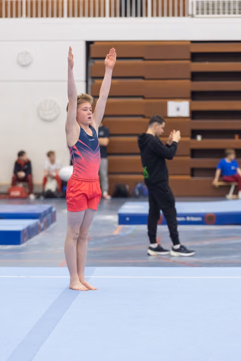 Young gymnast completes floor routine with arms raised high, showing concentration and poise in gymnasium