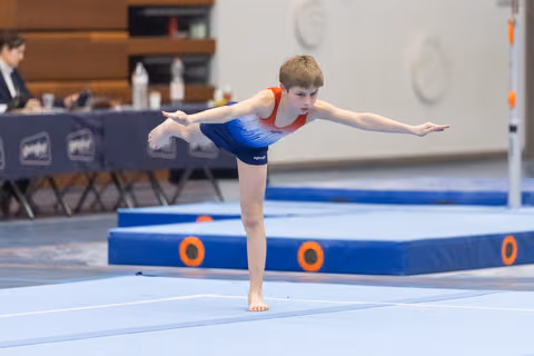 Young gymnast holds an arabesque balance during floor routine, arms extended gracefully, in a training facility