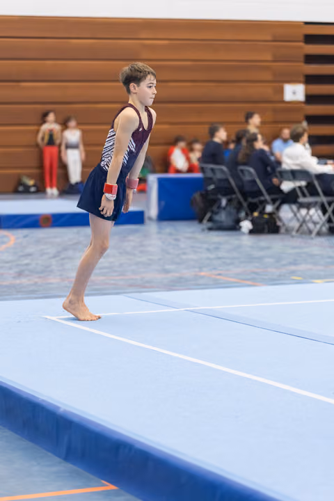 Young gymnast stands focused on floor mat, awaiting start of routine at indoor gymnastics meet
