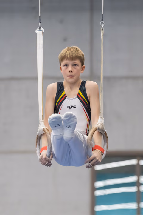 Young gymnast performing L-sit on rings, displaying intense concentration and controlled form during routine