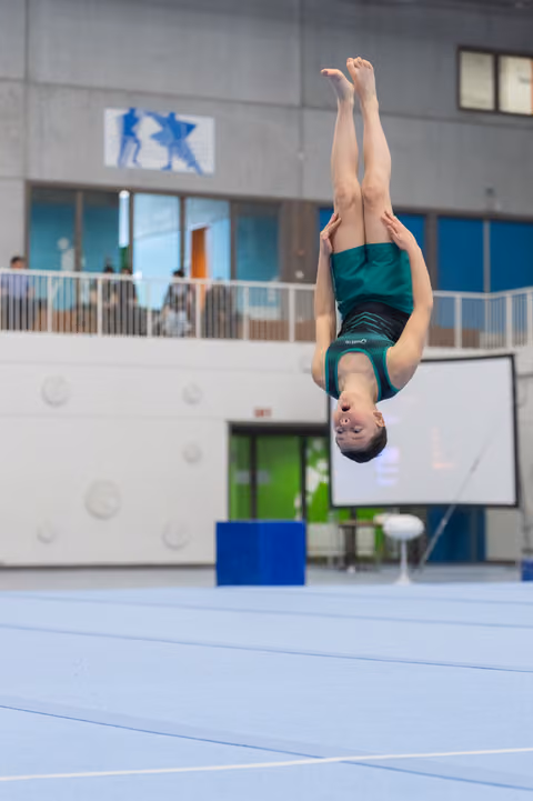 Gymnast performs vertical flip above floor mat with extended body position in indoor training facility