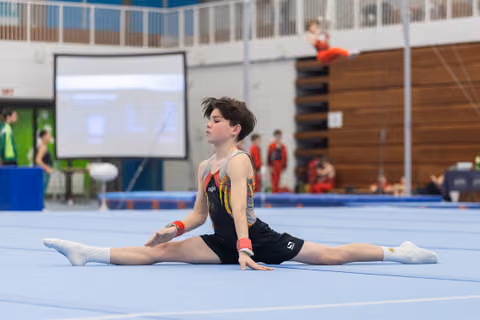 Young gymnast performs a splits position on floor exercise mat during routine at indoor gymnastics meet