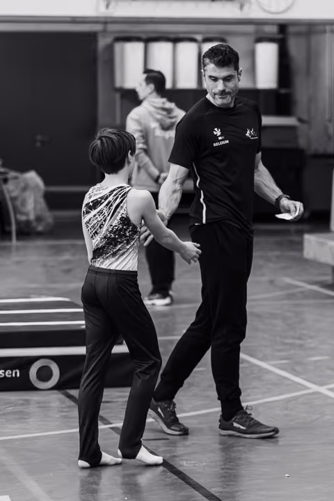 Smiling coach guides young gymnast in sequined leotard during floor exercise practice in training hall