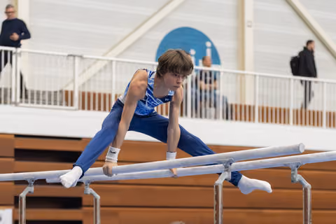 Young male gymnast in blue leotard performs on parallel bars, displaying strength and concentration during his routine