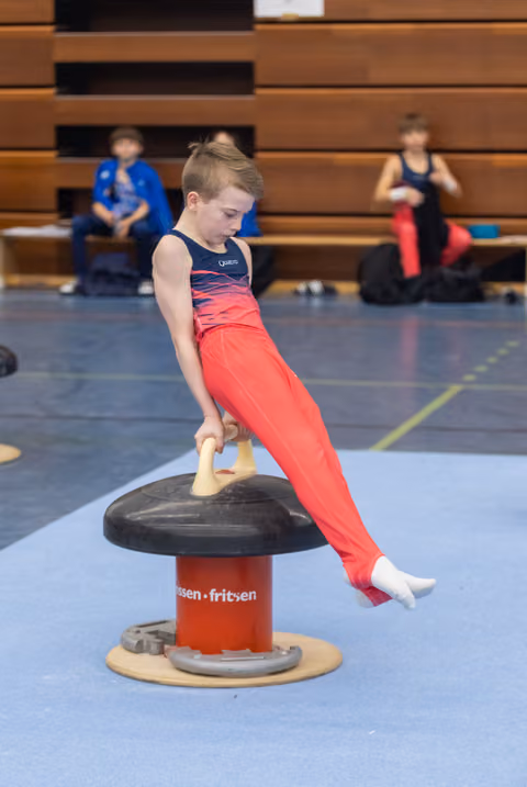 Young gymnast in red uniform executes a horizontal circle position on pommel mushroom apparatus during training session