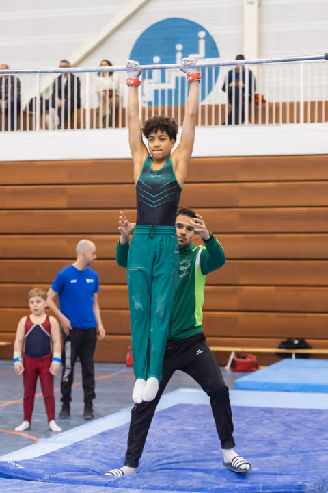 Young gymnast balances upright on coach's shoulders with arms raised, demonstrating acrobatic partnership in gymnasium