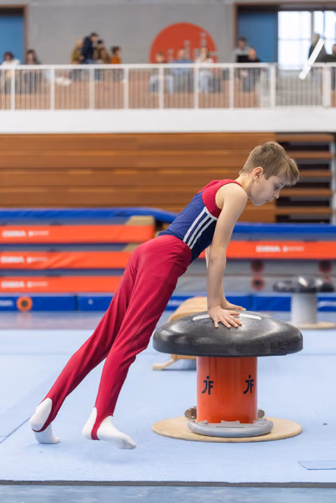 Young gymnast in burgundy and navy uniform performing a plank position on mushroom apparatus during training