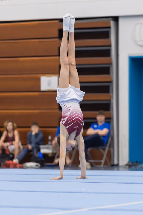 Gymnast performs a vertical handstand on floor exercise, demonstrating balance and control during routine at indoor competition