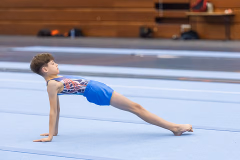 Young gymnast performs a reverse plank position with extended legs during floor routine in training facility