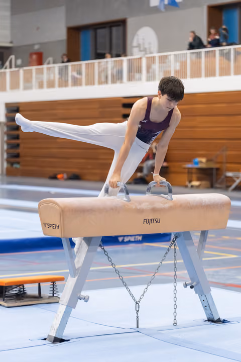 Young gymnast executes a scissor move on pommel horse, legs extended horizontally in focused concentration at training facility