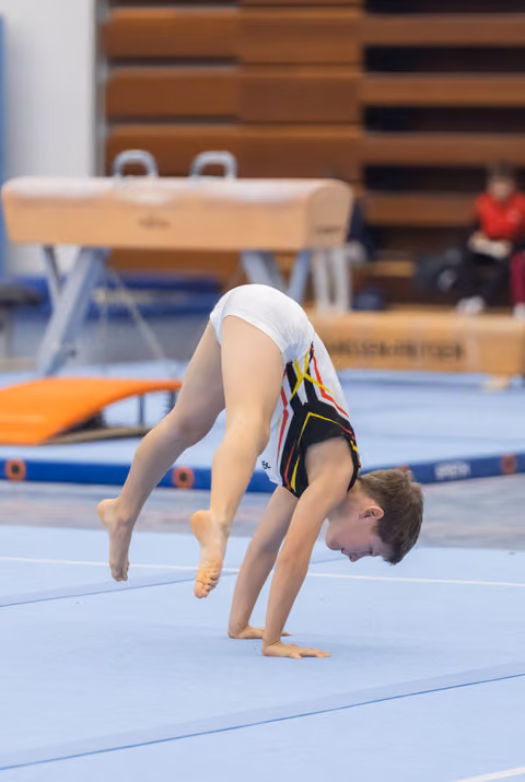 Young gymnast executes a deep backbend during floor routine, showcasing flexibility with head lowered and legs extended