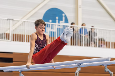 Young gymnast holds a V-sit position on parallel bars, displaying concentration and strength during training routine