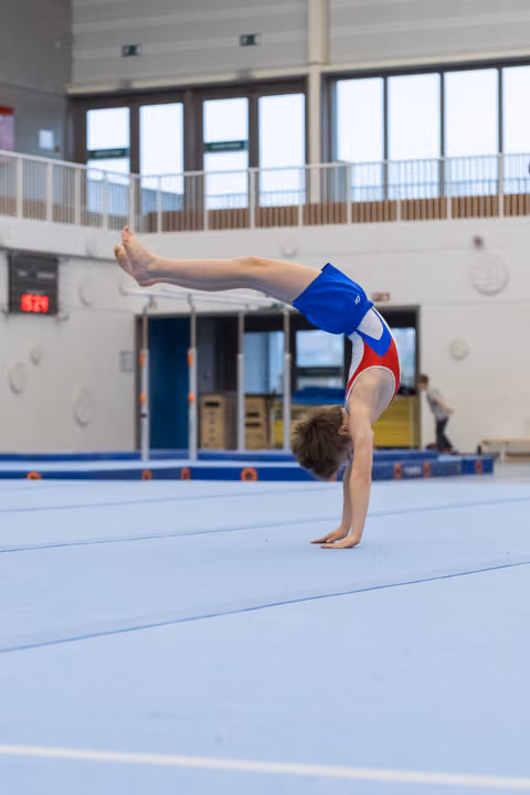 Young gymnast holds a precise handstand position on the blue floor mat, demonstrating strength and balance during training.