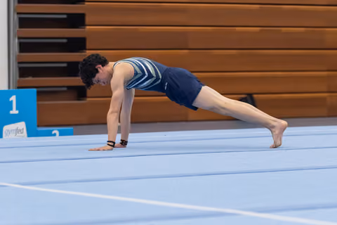Male gymnast holds a plank position on a blue gymnastics mat, demonstrating strength and control in a gym setting