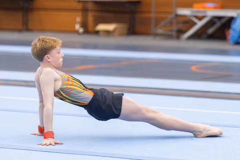 Young gymnast in colorful leotard holds a reverse plank position on the floor mat, demonstrating strength and control