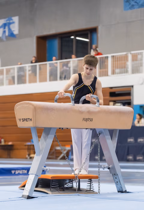 Young gymnast grips pommel horse handles, focused and ready to begin his routine in indoor sports hall