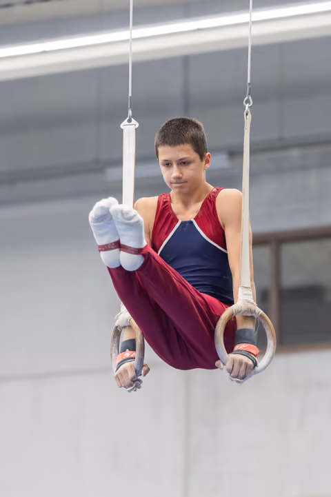 Young gymnast performing an L-sit position on rings, demonstrating focused concentration and core strength in training facility