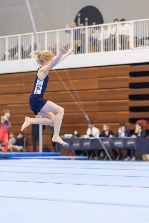 Young gymnast in navy leotard performs an elegant leap during floor exercise routine at indoor gymnastics meet