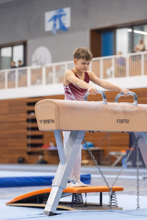 Young gymnast grips pommel horse handles with focused concentration, preparing for his routine in indoor training facility
