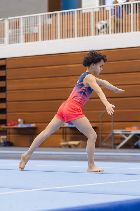 Young gymnast performs graceful leap position during floor routine, arms extended with focused expression in training gym